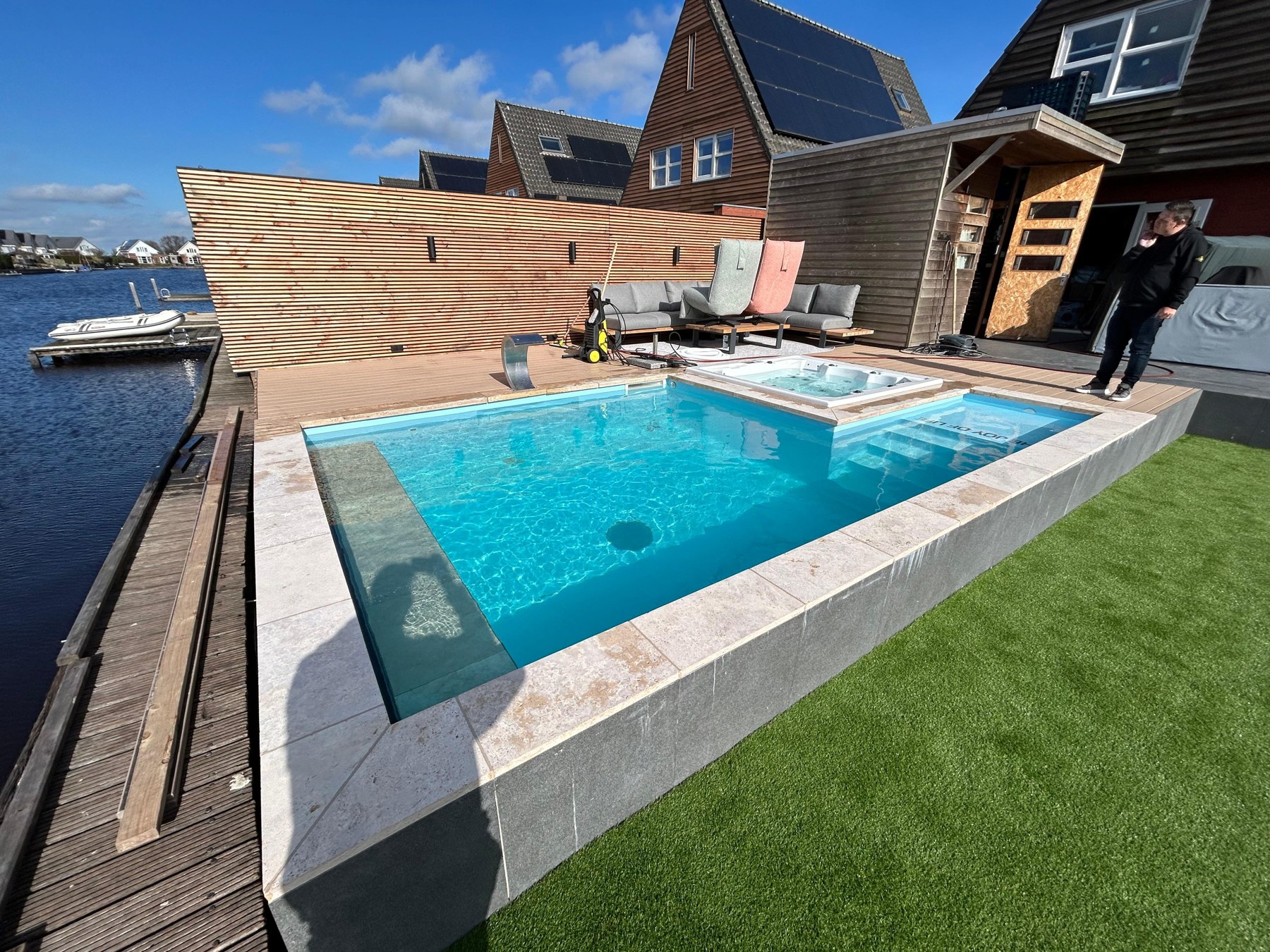 Overzicht van zwembad en ingebouwde spa aan het water in Nes, met terras en gazon.