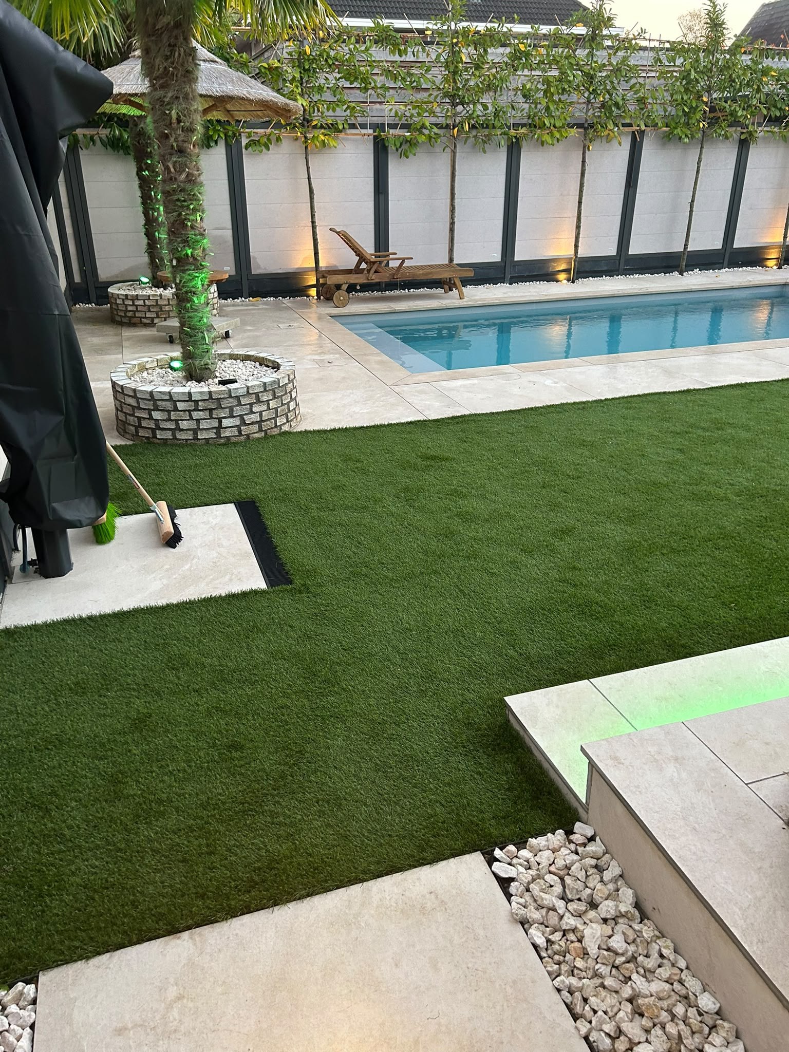 Zwembad met lichte randstenen, gazon en palmen in een tuin in Enschede.
