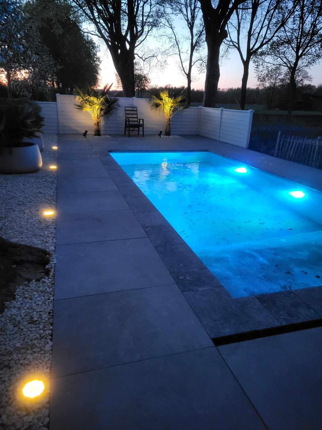 Zwembad met blauwe verlichting en brede betegelde rand in Doornspijk.