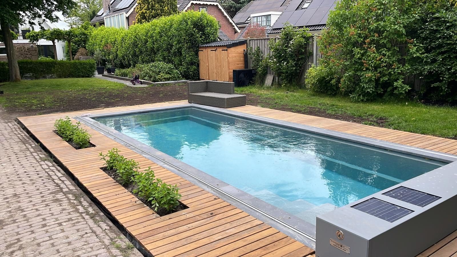 Zwembad met houten terras en plantvakken in een groene tuin in Oosterblokker.