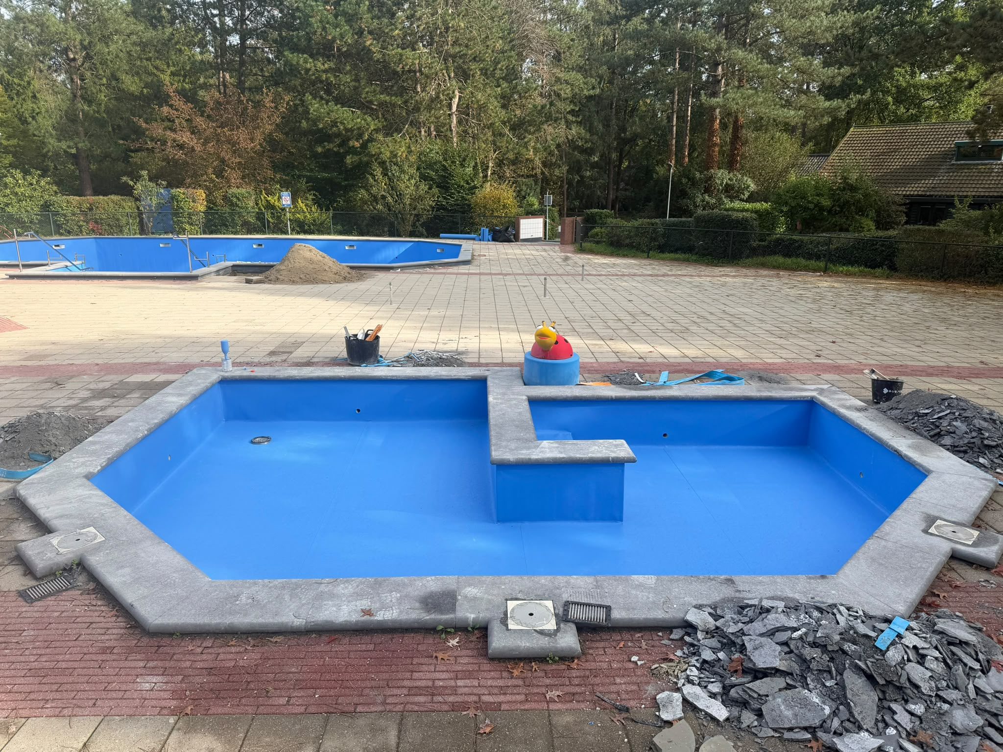 Kleiner blauw buitenbad met het grote zwembad op de achtergrond tijdens werkzaamheden. · foto 1