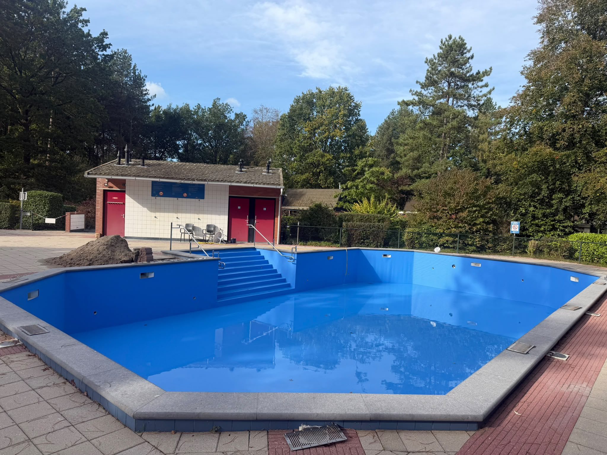 Groot blauw buitenbad met brede trap en leuningen in een groene omgeving.