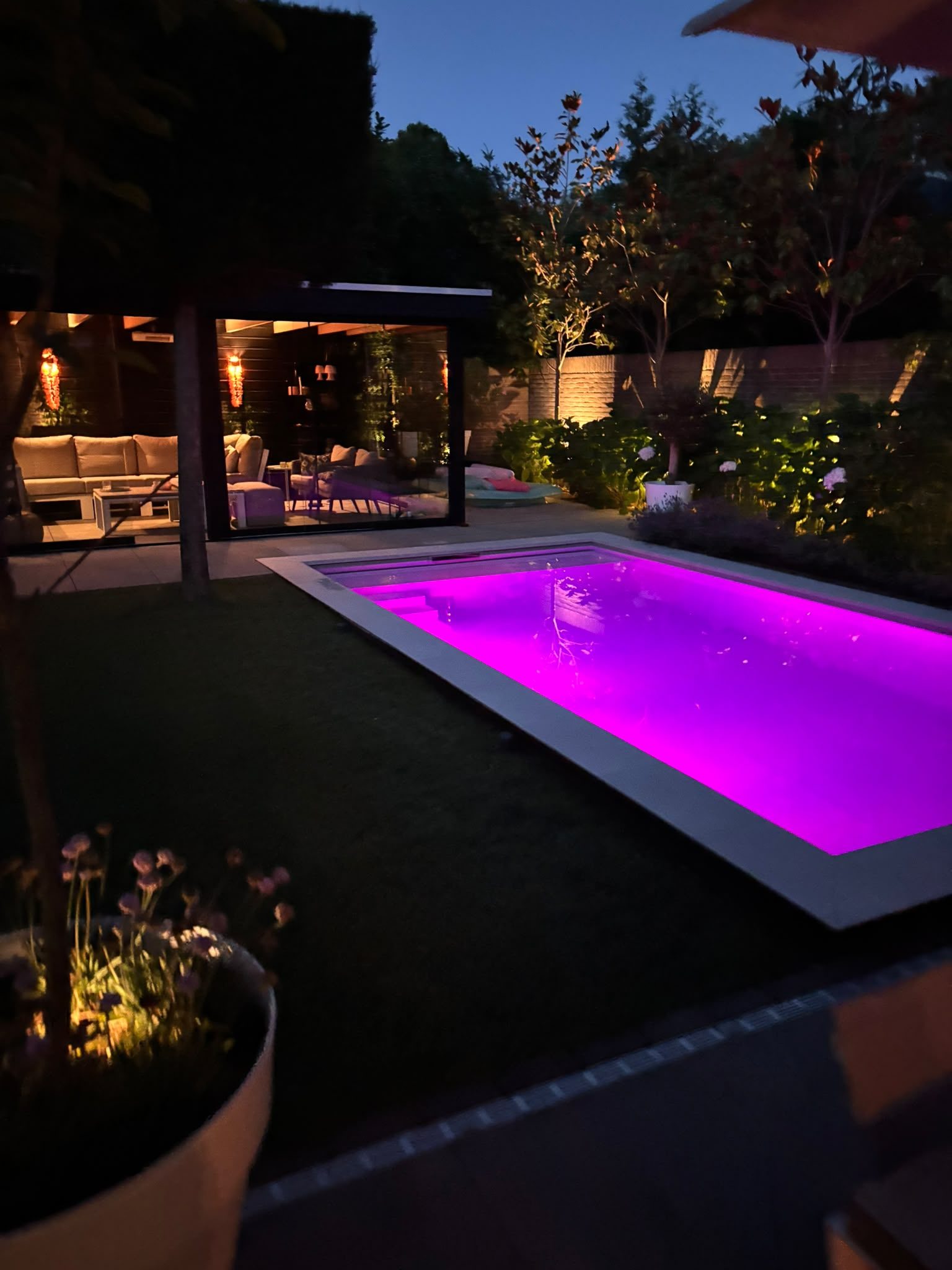 Zwembad met paarse verlichting en een verlicht poolhouse in Oss bij avond.